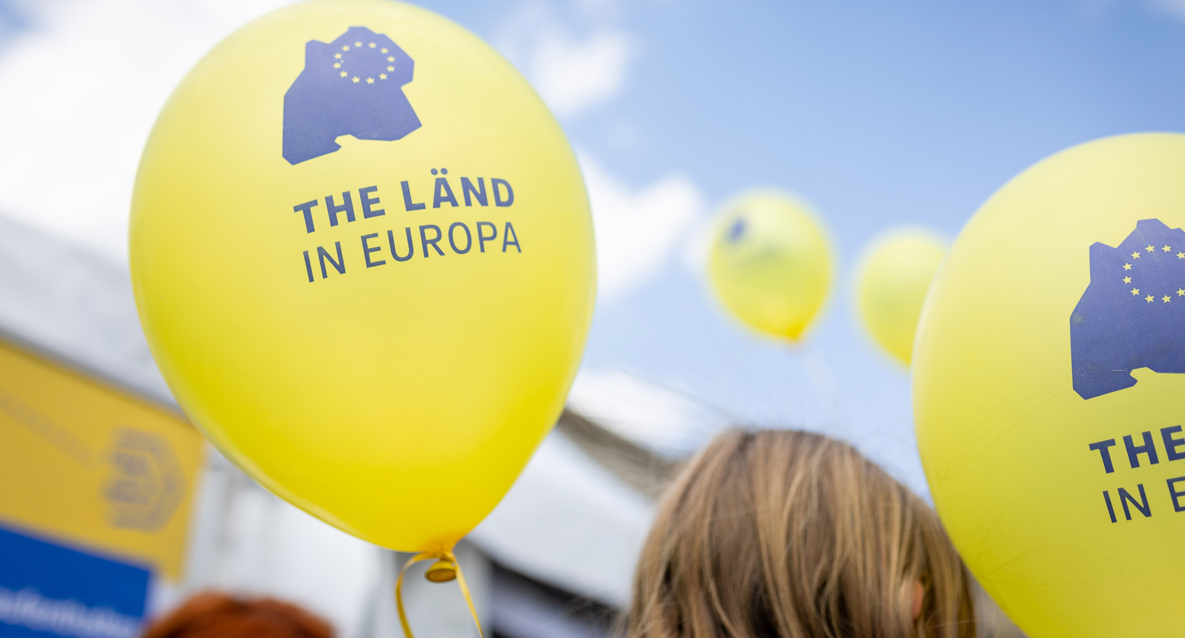 Gelbe Luftballons mit blauer Aufschrift &bdquo;THE L&Auml;ND IN EUROPA&ldquo;