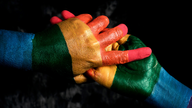 Zwei ineinandergreifende H&auml;nde in den Regenbogenfarben der LSBTQIA+-Community.